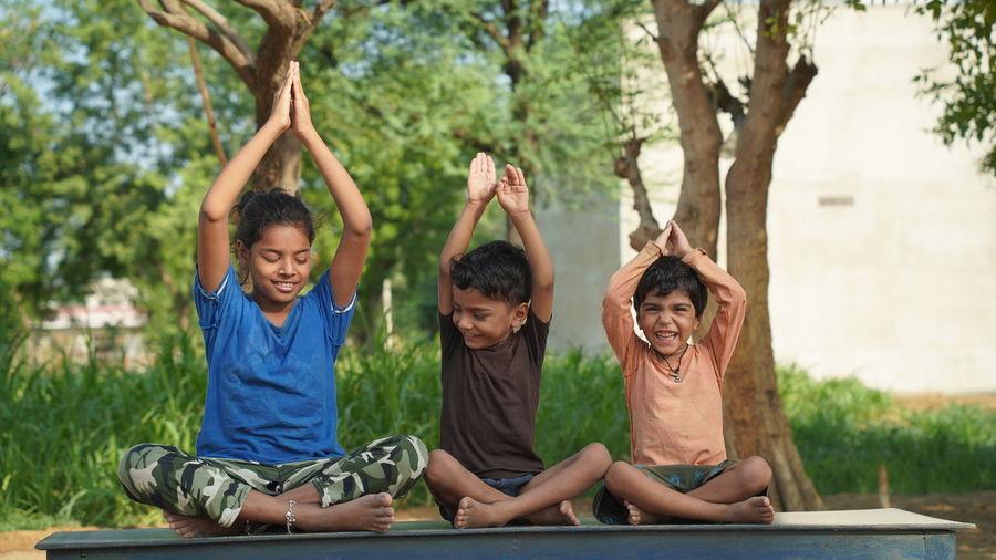 Two indian little girl and a boy doing meditate yoga asana on roll mat with eyes closed in park.