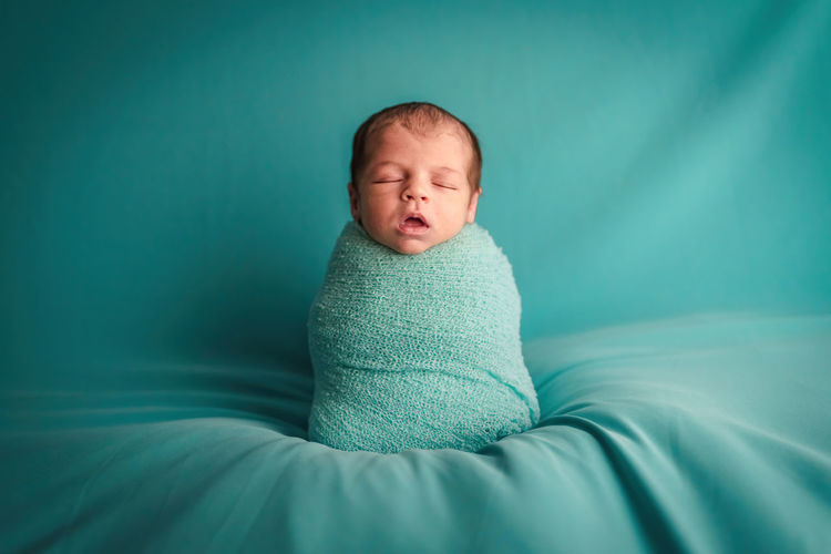 Newborn baby sleeping peacefully in a in a turquoise wool ball. newborn session concept