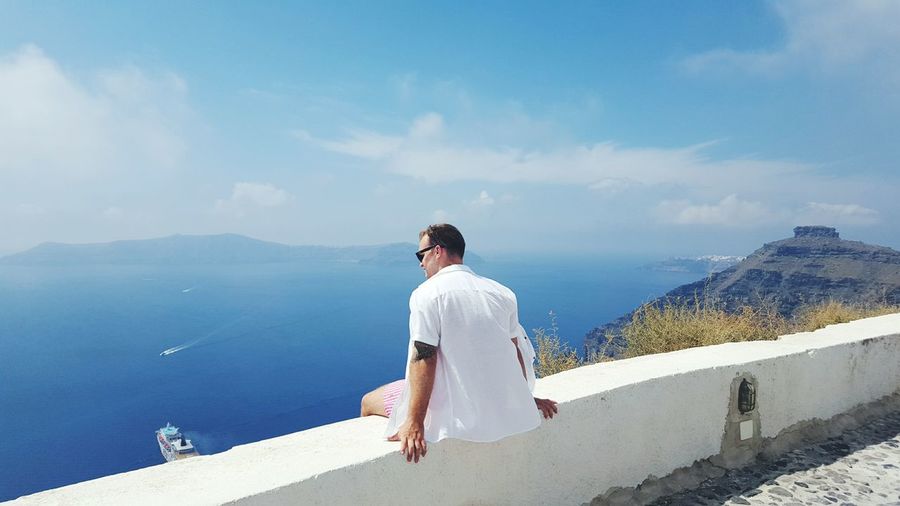 Man sitting on wall at beach against sky