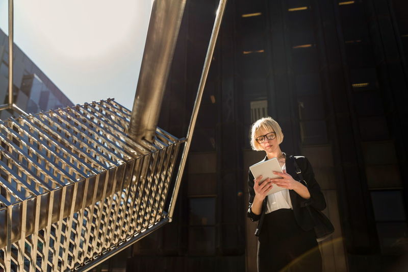 Stylish attractive businesswoman standing and browsing digital tablet on street