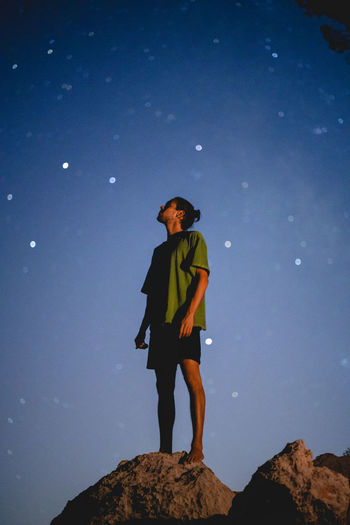 Low angle view of man standing on rock against night sky