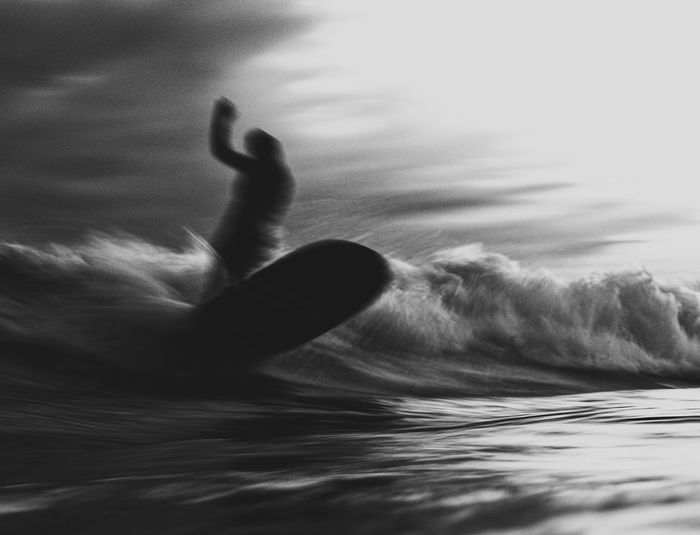 Blurred image of person surfing in sea against sky