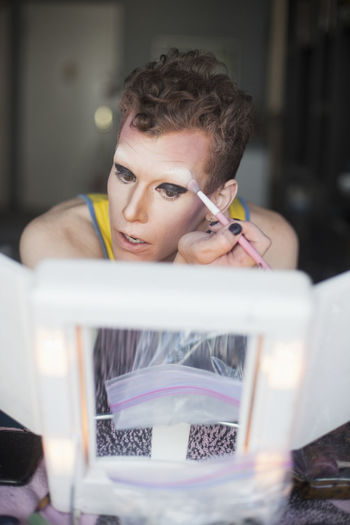 Man looking in mirror and applying drag cosmetics