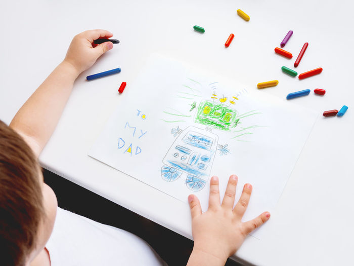 Left-handed toddler draws greeting card with funny robot for father's day or daddy's birthday. 
