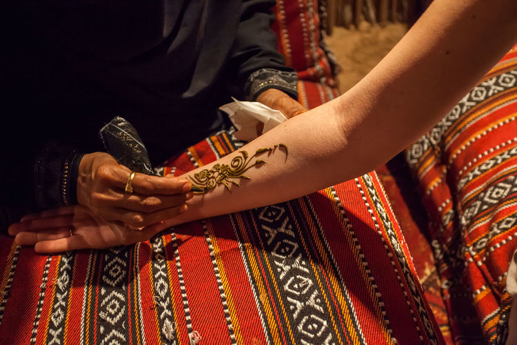 Midsection of woman applying henna tattoo on customer hand