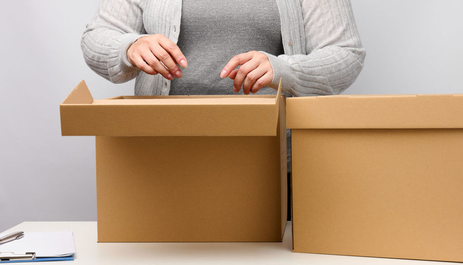 Woman in gray clothes stands and holds open brown box on a white background, moving, 