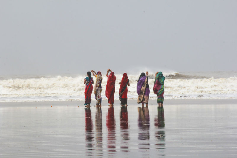 Rear view of women performing rituals while standing on wet shore