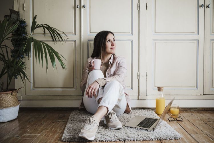 Thoughtful businesswoman looking away while sitting on rug at home