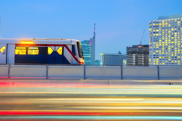 Bangkok sky train with cityscape and light trail motion from vehicle on road on evening time