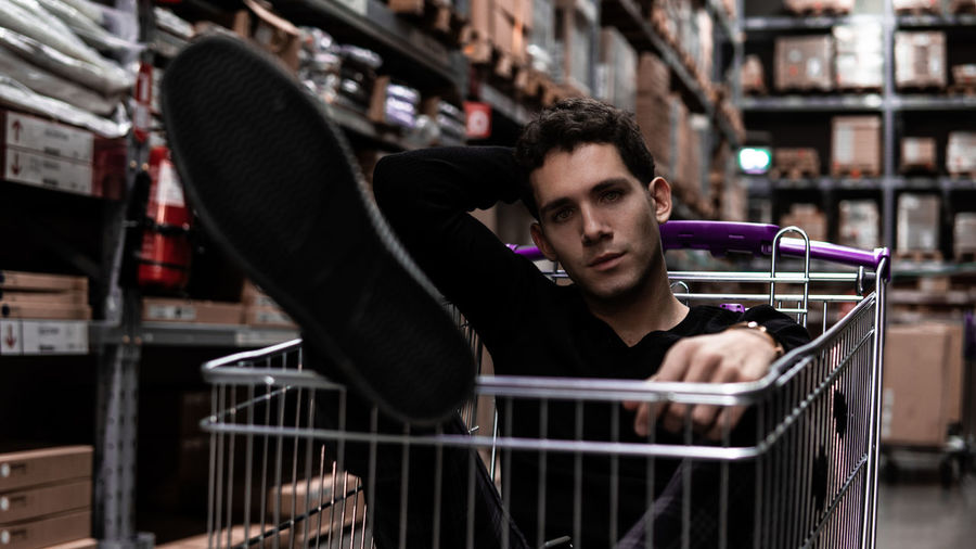 Portrait of young man sitting in shopping cart at store