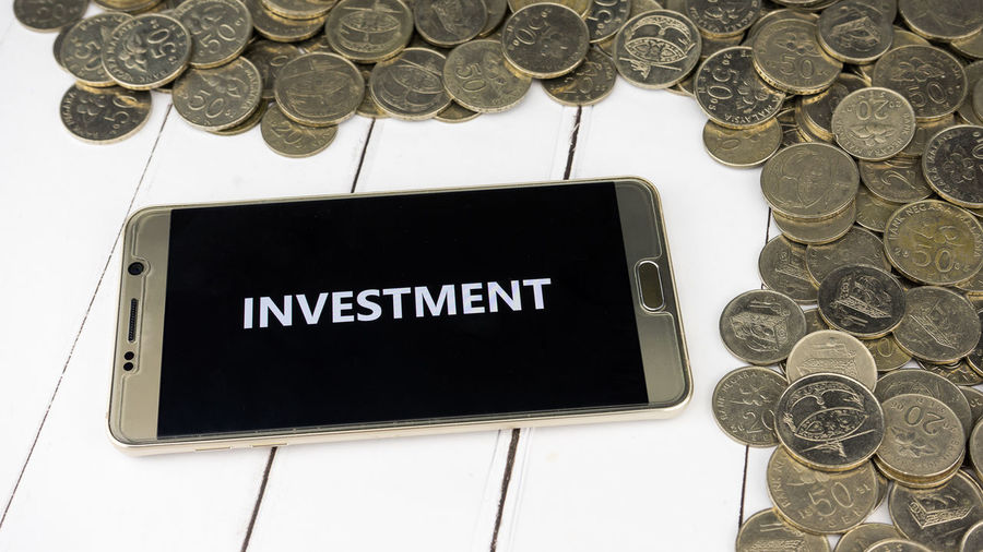 High angle view of investment text in smart phone by coins on table