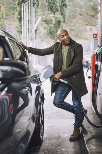 Mature man looking away while refueling car standing at gas station