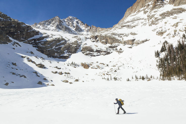Woman hikes across frozen black lake, rocky mountain national park