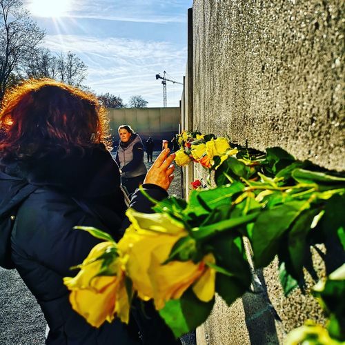 Rear view of people standing by flowering plants against sky