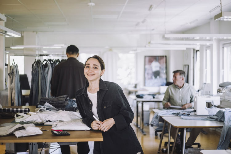Portrait of smiling young fashion designer leaning on workbench at workshop