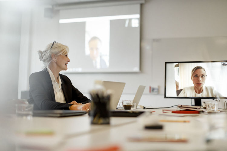 Smiling businesswoman listening to female professional through video conference in board room at office