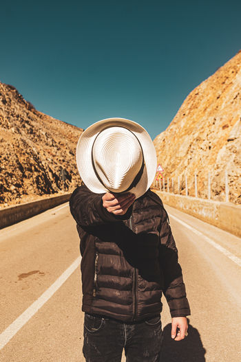 Man wearing hat standing by road against clear sky