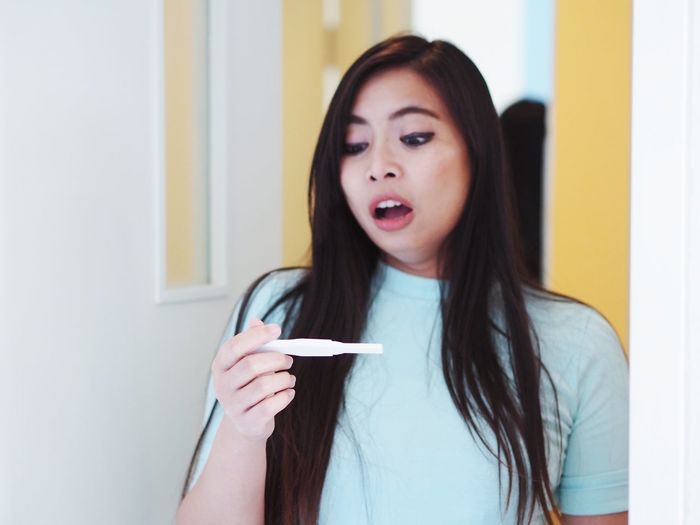 Surprised young woman holding pregnancy test equipment at home