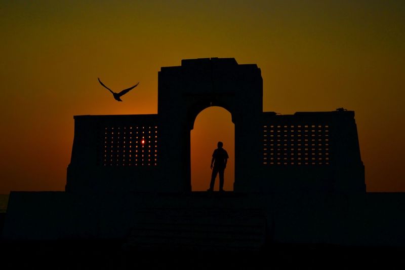 Silhouette man standing by building against sky during sunset