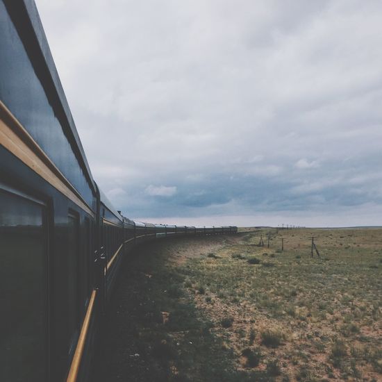 Train passing by field against cloudy sky