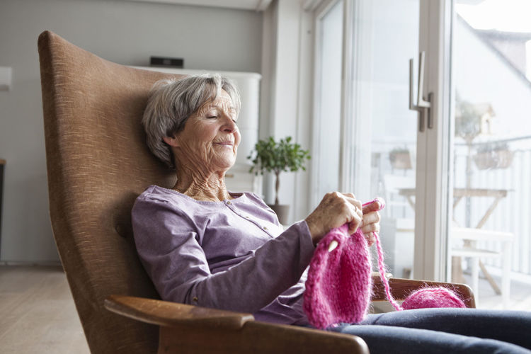 Portrait of senior woman sitting on armchair at home knitting