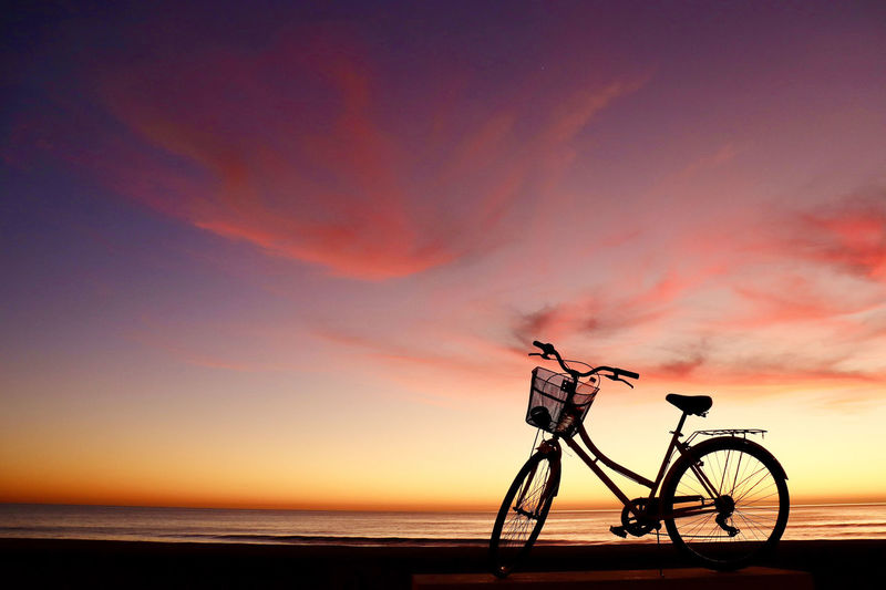 Silhouette bicycle on beach against sky during sunset
