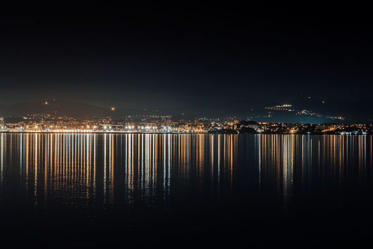 Illuminated city by sea against clear sky at night