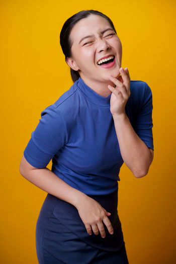 Happy woman standing against yellow background