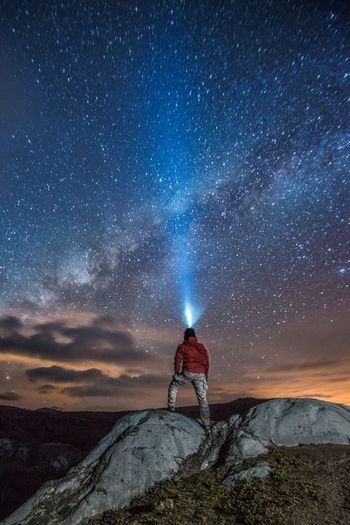 Man with illuminated headlamp standing on rock against milky way