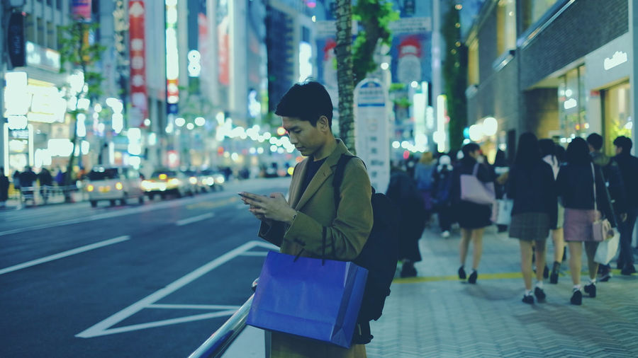 Man using smart phone while standing on street in city