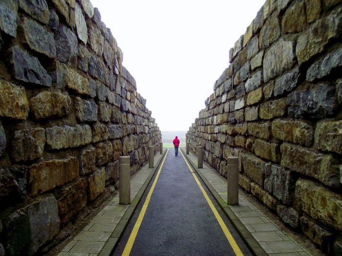 Rear view full length of person walking amidst stone walls