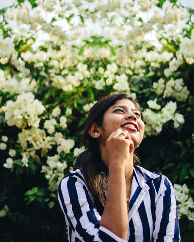 Portrait of smiling young woman looking away outdoors under white flowers 