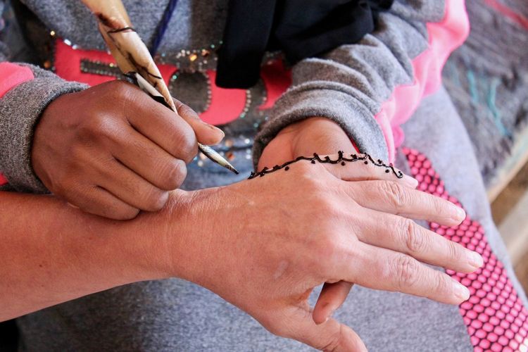 Midsection of artist making henna tattoo on hand of woman