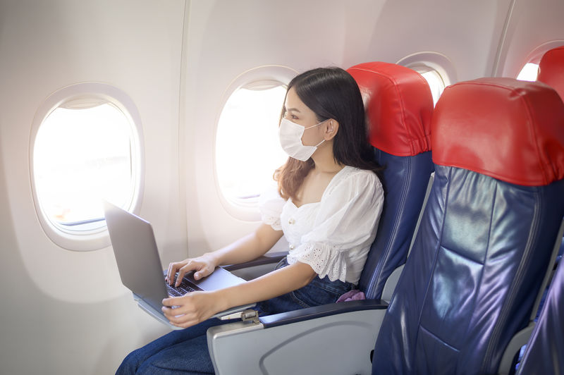 Woman wearing flu mask working on laptop sitting in plane