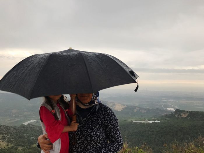 Mother and daughter under umbrella against sky during sunset
