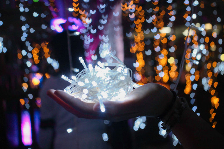 Close-up cropped hand holding of illuminated christmas lights