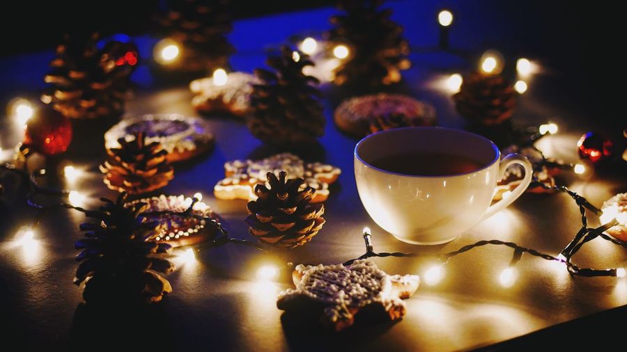 Close-up of coffee cup and gingerbread cookies amidst illuminated christmas lights