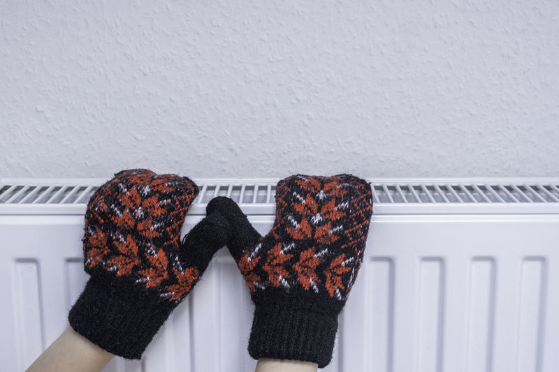Hands in mittens on the radiator. low temperature in houses in winter.