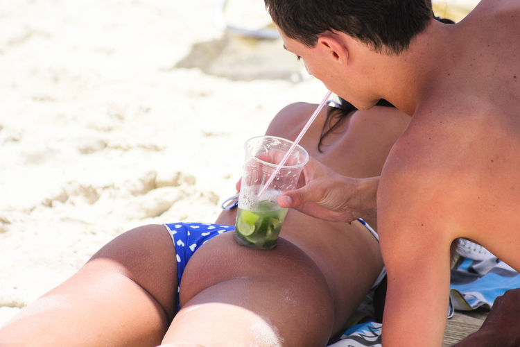 Young man having drink on girlfriend buttocks at beach