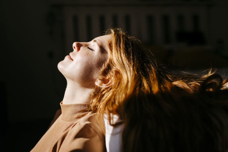 Smiling woman leaning head at home in sunlight