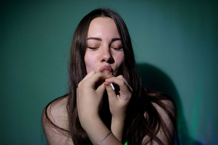 Beautiful young woman with eyes closed licking lollipop
