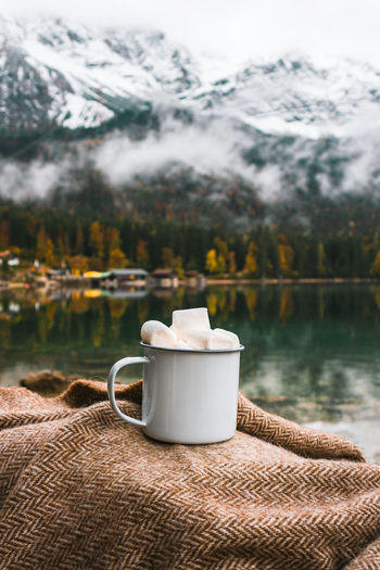 Picnic in bavarian mountains, germany. mug of cacao and marshmallow on the lake background