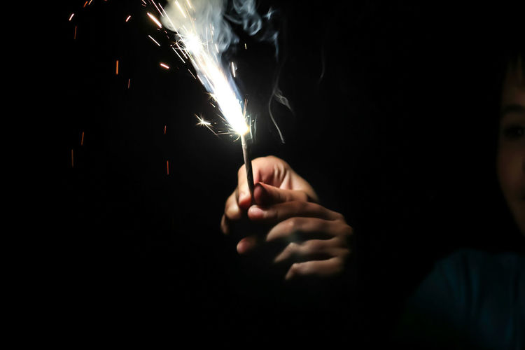 Cropped image of person holding illuminated sparkle against black background