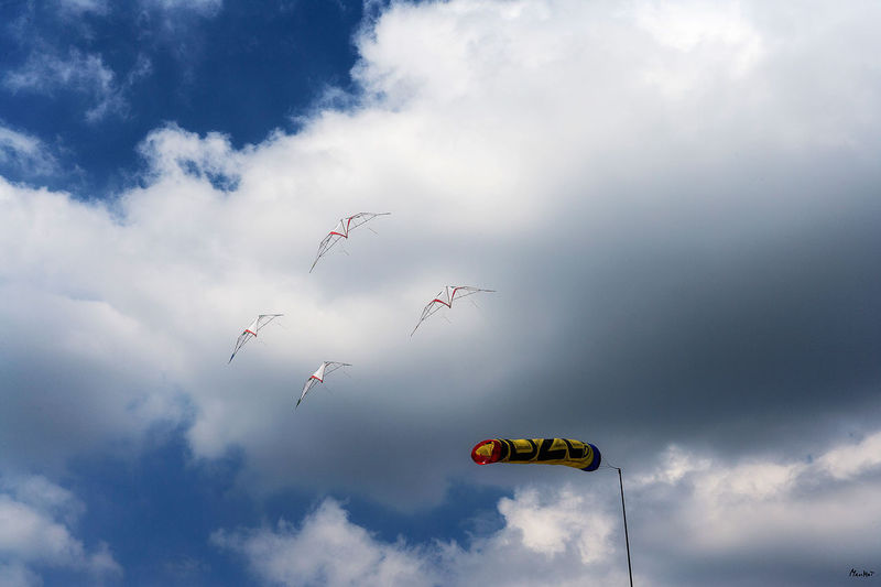 Low angle view of kites flying and windsock in sky