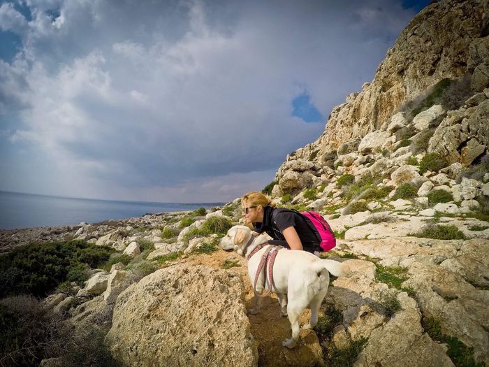 Woman with dog on rock against sky