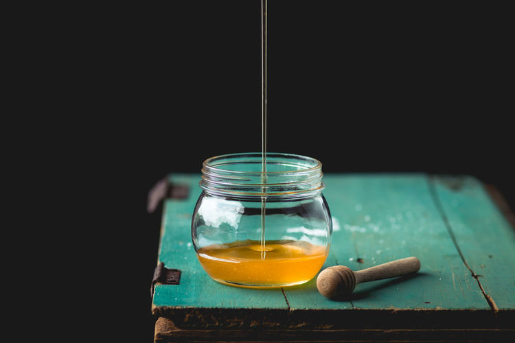 Close-up of honey falling in glass jar on table against black background