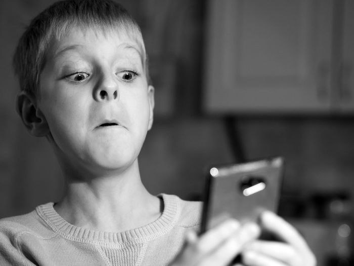Close-up of shocked boy using phone at home