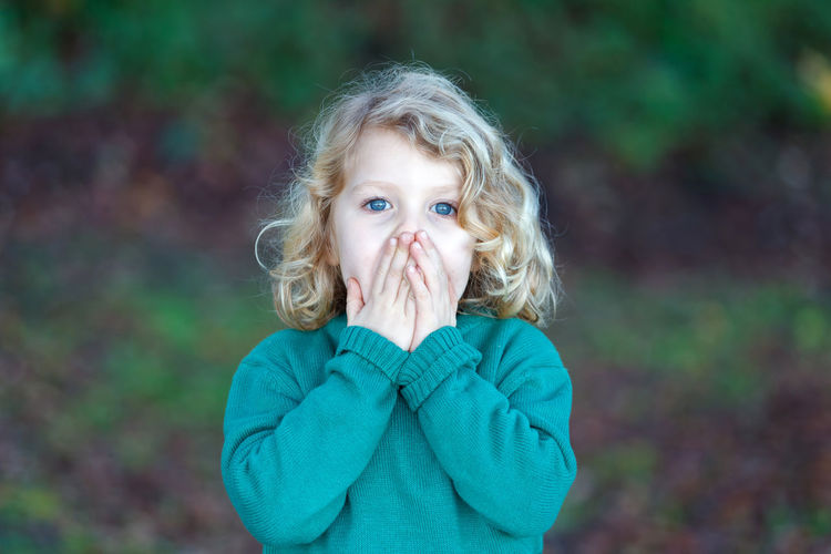 Portrait of cute girl with hands covering mouth standing in park