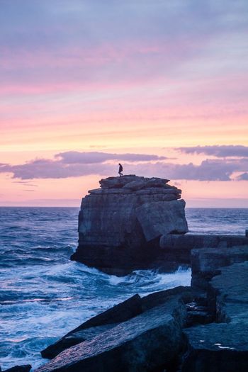 Distant view of silhouette person on cliff by sea against sky