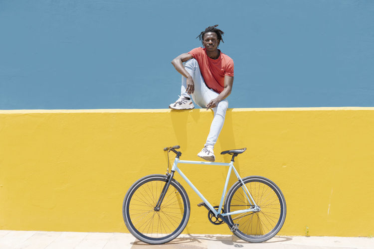 Full length of man riding bicycle against yellow wall